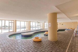 Una piscina interior con suelo de baldosas, un jacuzzi y un pilar grande.