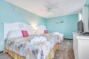 A room with two beds, a ceiling fan, a television on a cabinet, and a wall with a painting. - Luxury Oceanfront 3BR w/ Hot Tub & Stunning View (Myrtle Beach)