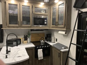 A compact kitchen with wooden cabinets, a built-in microwave, a stove, and a coffee maker.
