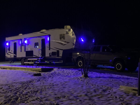 A camper trailer with a flatbed attached to a pickup truck parked on a snow-covered ground.