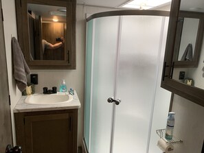 A bathroom with a white sink, a mirror, a shower with frosted glass doors, and a towel hanging on the wall.
