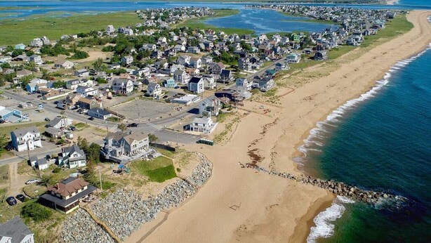A coastal residential area with houses along the beach and a road running parallel to the shore.