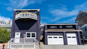 A two-story building with a balcony on the upper floor, a garage with two doors, and a white picket fence in front.