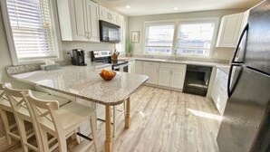 A kitchen with a granite countertop, white cabinets, a stainless steel refrigerator, and a wooden dining table with chairs.
