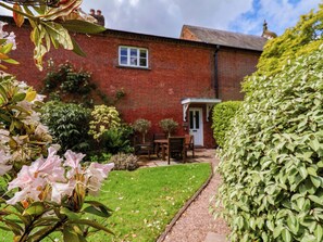 A brick house with a front door, a small porch, and a lawn with various plants. - Carriage House (Macclesfield)