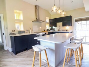 A modern kitchen with a central island, bar stools, a range of appliances, and pendant lighting. - Carriage House (Macclesfield)