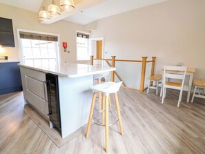 A modern kitchen with a central island, wooden stools, and a dining area with a small table and chairs. - Carriage House (Macclesfield)