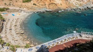 An aerial view of a beach with clear turquoise waters, a rocky shoreline, and a series of sun loungers and umbrellas.