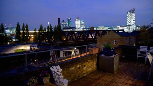 A rooftop terrace with a view of a city skyline at dusk, featuring a bridge and modern buildings. - Large Shoreditch 2/dbl bed Loft apt (London)