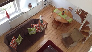 A living room with a brown sofa, a dining table with four chairs, and a staircase. - Large Shoreditch 2/dbl bed Loft apt (London)