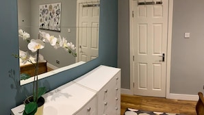 Quarto com penteadeira branca, espelho, planta em vaso e porta com moldura branca.