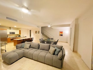 A modern living room with a sectional sofa, a dining area with a glass table, and a kitchen with a microwave and stove. - Steps from Beach Club, Pools, Restaurants, Shopping and the Pacific!! (El Chirú)