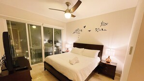 A bedroom with a bed, a ceiling fan, a nightstand, a lamp, and a TV.