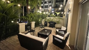 An outdoor patio area with seating arrangements, including sofas and chairs, surrounded by potted plants and string lights.
