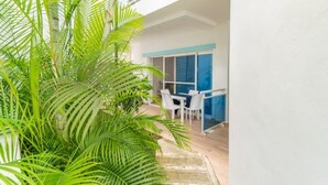 Ein modernes Hotelzimmer mit Balkon, einer Essecke mit weißen Stühlen und üppiger, grüner Bepflanzung.