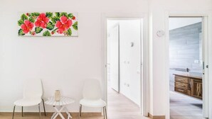 Ein modernes Zimmer mit weißer Wand, einem Gemälde von roten Blumen, zwei weißen Stühlen, einem kleinen runden Tisch und Holzboden.