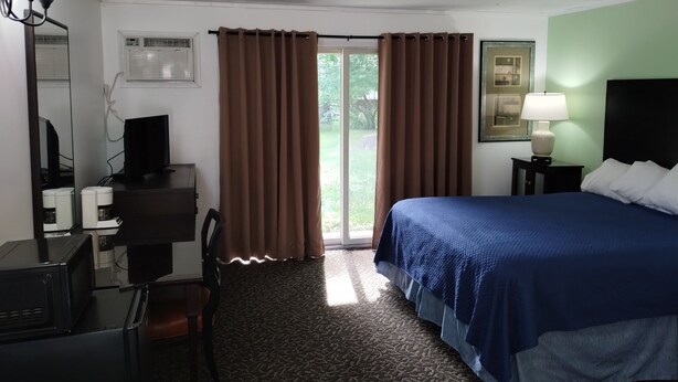 Une chambre d’hôtel avec un lit, un bureau équipé d’un ordinateur, une chaise, une lampe et une fenêtre avec des rideaux.