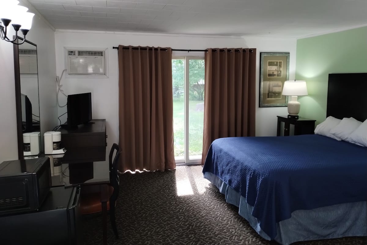 Habitación de hotel con cama, escritorio, computadora, silla, lámpara y ventana con cortinas.