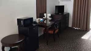 Une chambre d’hôtel équipée d’un bureau, d’une chaise, d’un petit réfrigérateur, d’un four à micro-ondes, d’une télévision, d’un miroir, d’une machine à café et d’une fenêtre avec des rideaux.