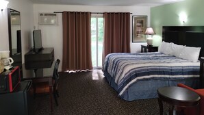 Une chambre d’hôtel avec un lit, un bureau avec un ordinateur, une chaise, une petite table et une fenêtre avec des rideaux.