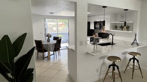 Une cuisine moderne avec des meubles blancs, un micro-ondes noir et un évier avec un robinet doré. On y trouve deux tabourets et un vase avec des fleurs sur le comptoir.