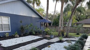 Un jardin résidentiel avec un espace patio, une variété de plantes et une maison en arrière-plan.