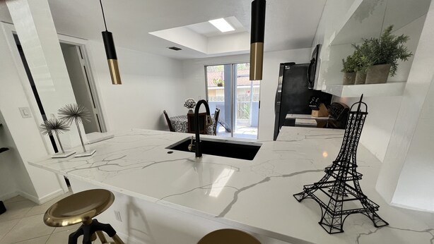 Une cuisine moderne avec un plan de travail en marbre blanc, des tabourets de bar dorés, des luminaires suspendus et une maquette de la Tour Eiffel noire.