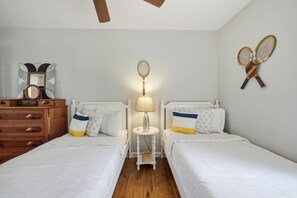 Een slaapkamer met twee bedden, een kaptafel, een lamp en tennisrackets aan de muur.
