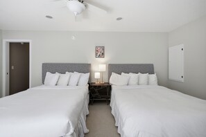 A hotel room with two beds, a ceiling fan, a nightstand with a lamp, and a framed picture on the wall.