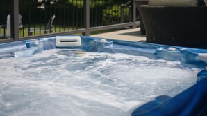 A hot tub with visible bubbles, a metal railing, and a wicker chair in the background. - Union Pier Home Walking Distance To Beach With Hot Tub! (Union Pier)