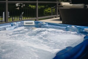 A hot tub with visible bubbles, a metal railing, and a wicker chair in the background.