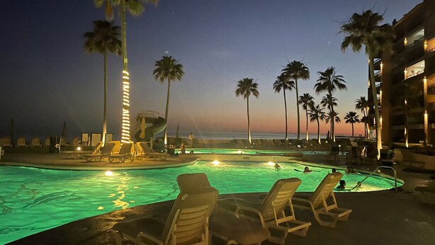 A pool area with lounge chairs, palm trees, and a building with balconies overlooking the pool. - Beachfront Lower Floor Luxury Condo (Puerto Peñasco)