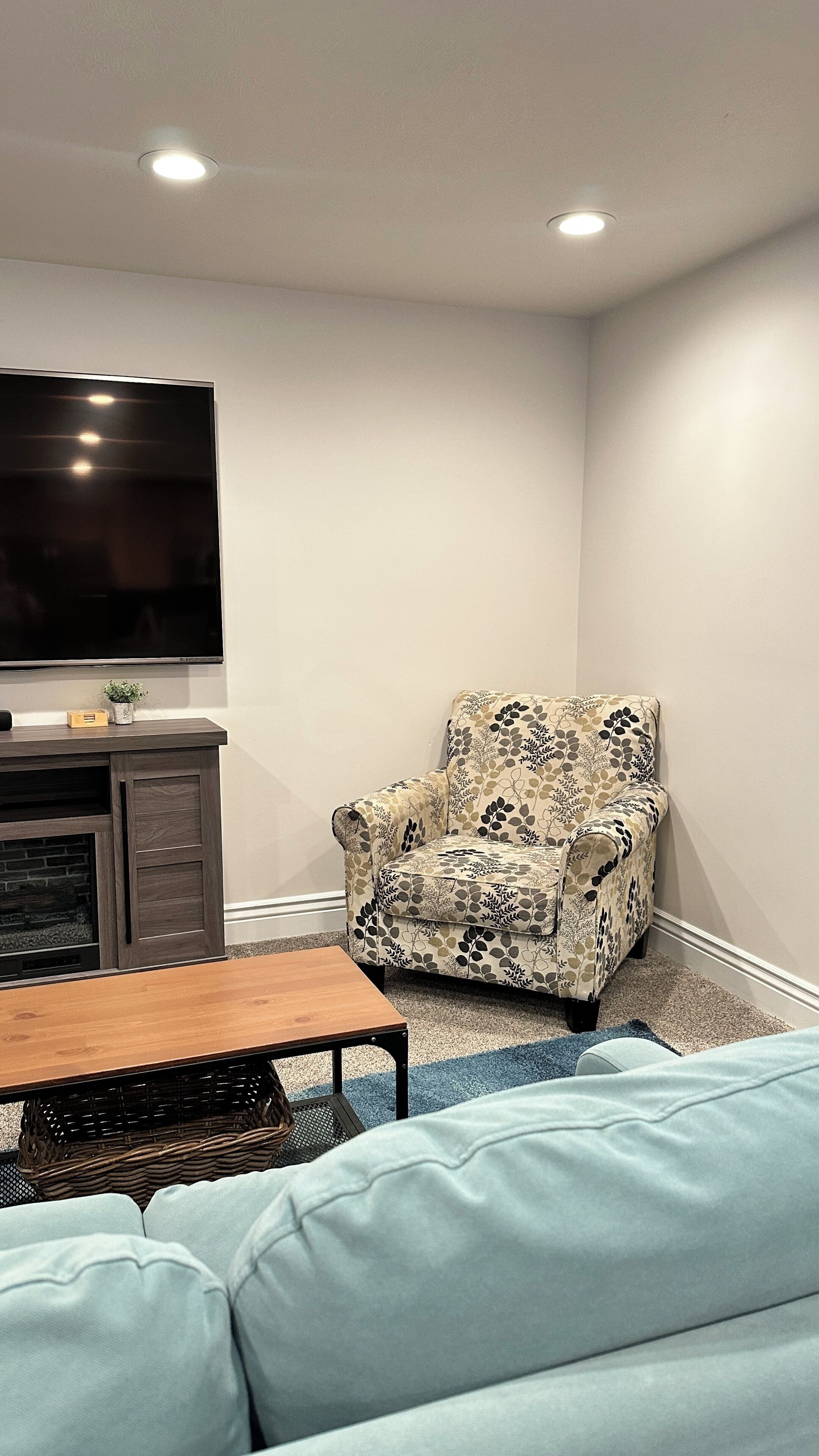 A living room with a sofa, a patterned armchair, a flat-screen TV, a wooden coffee table, and a fireplace.