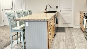 Een keuken met een centraal eiland, twee dubbele deuren en een eetgedeelte met stoelen.