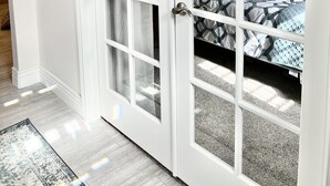 Een kamer met een grote schuifdeur die leidt naar een slaapkamer. De vloer is licht van kleur en er ligt een vloerkleed.