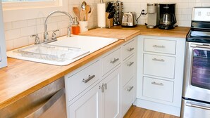 Een moderne keuken met witte kasten, een houten aanrechtblad, een roestvrijstalen spoelbak en een ingebouwde oven.