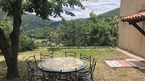 Mesa redonda con sillas de metal, rodeada por un área verde con un árbol y vistas a un paisaje montañoso.