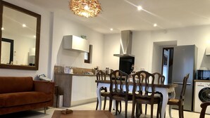 Una sala de estar moderna con un sofá marrón, una mesa de comedor de madera y sillas, una cocina con horno empotrado y microondas, y un espejo grande en la pared.