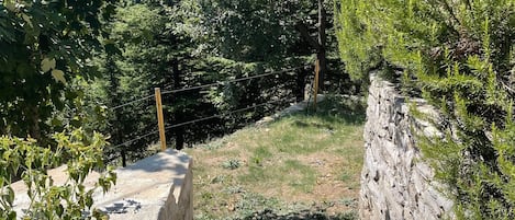 Una scalinata in pietra conduce su un pendio, circondata da vegetazione lussureggiante e un cielo sereno.