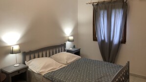 Un dormitorio con cama, dos mesitas de noche, lámpara, ventana con cortinas e iluminación en el techo.