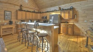 A wooden cabin kitchen with a central island, bar stools, wooden cabinets, a refrigerator, and a microwave. - Downtown Lodge Blue Ridge, sleeps 14,walk to strip (Blue Ridge)