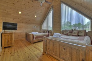 Camera da letto in una baita di legno con due letti, una televisione e ampie finestre.