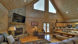A cozy cabin interior with a stone fireplace, wooden walls, a large window, and a kitchen area. - Downtown Lodge Blue Ridge, sleeps 14,walk to strip (Blue Ridge)