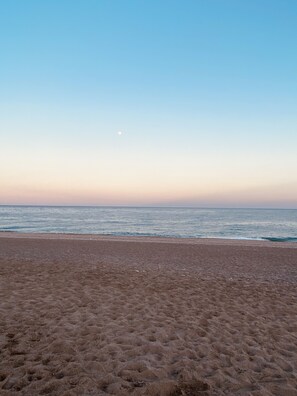 Une plage avec un ciel dégagé et une lune bien visible.