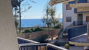 A balcony with a view of the sea, a building with a blue and white striped awning, and a staircase leading to an upper level. - Beautiful, newly remodeled 1 bedroom -50 meters from the beach (Giardini-naxos)