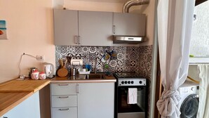 A compact kitchen with grey cabinets, a tiled backsplash, a stove, and a washing machine. - Beautiful, newly remodeled 1 bedroom -50 meters from the beach (Giardini-naxos)