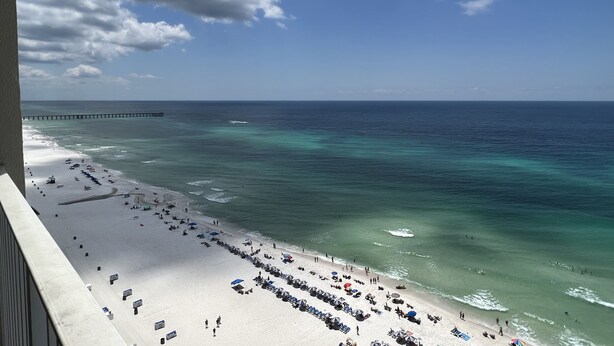 A beach with a pier extending into the ocean, a sandy shore with umbrellas and beach chairs, and a clear sky.