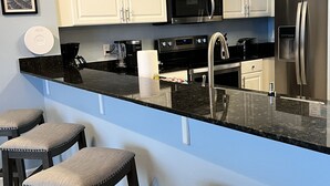 A modern kitchen with white cabinets, a black countertop, stainless steel appliances, and three bar stools.