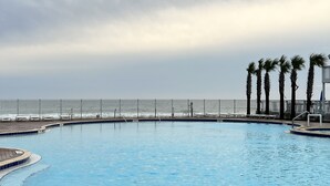 A swimming pool with a brick border, palm trees, and a view of the ocean.