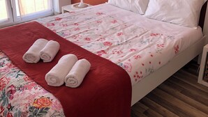Ein ordentlich gemachtes Bett mit floralem Überwurf und zwei aufgerollten Handtüchern auf einer roten Decke.